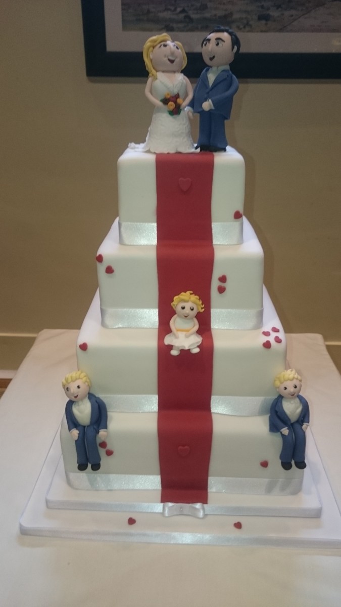 4 tier white wedding cake with red stripe and models of family members