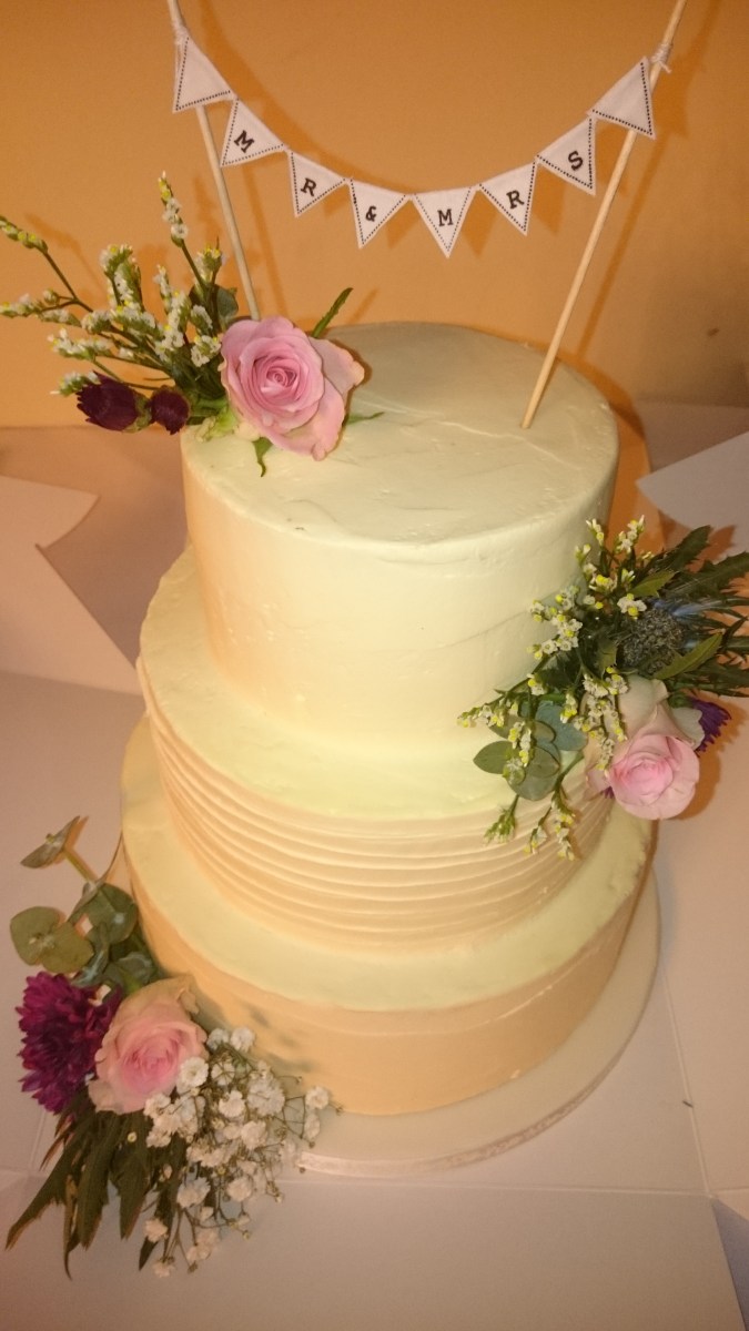 3 tier buttercream wedding cake with fresh roses, foliage and bunting