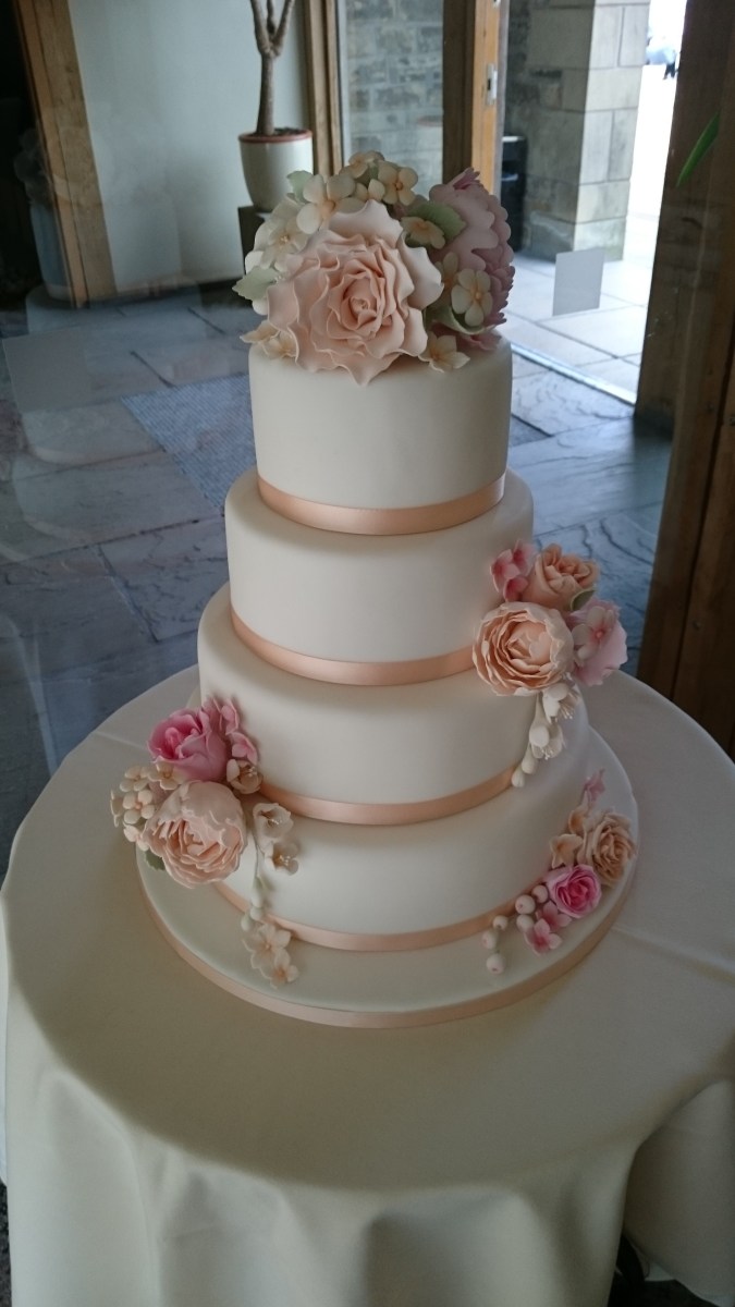 4 tier white wedding cake with peach ribbon and handmade sugar flowers