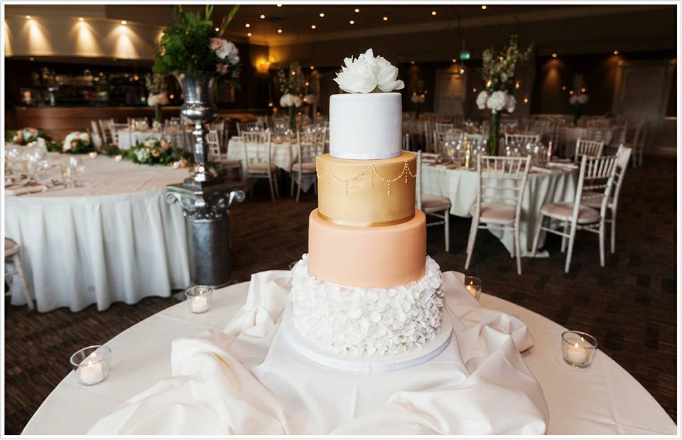 4 tier white, peach and gold wedding cake with ruffles and sugar flowers