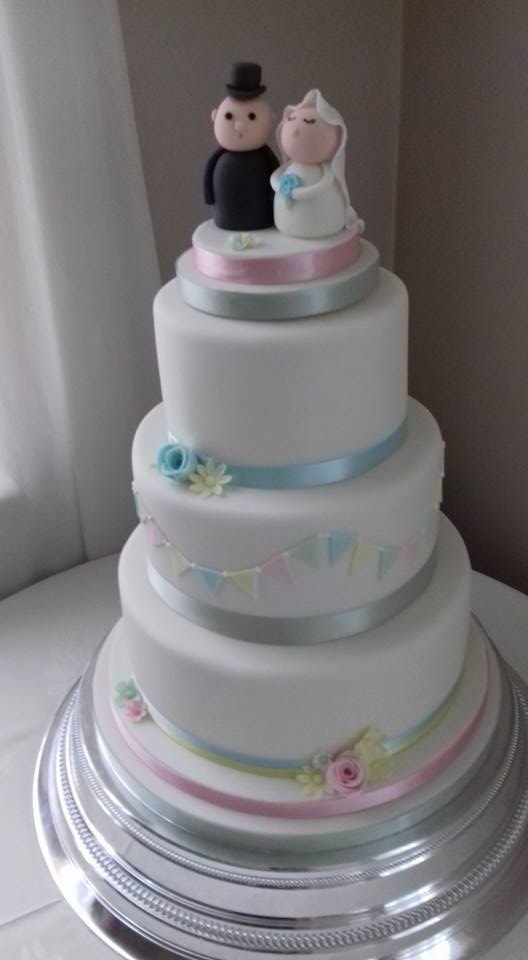 3 tier white wedding cake with bunting, flowers and bride and groom topper