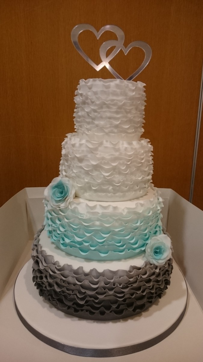 4 tier wedding cake with grey, blue and white graduated ruffles and handmade sugar flowers