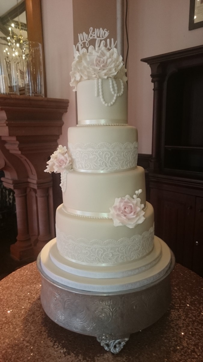 4 tier white wedding cake with pink ribbon, handmade sugar flowers and cake lace